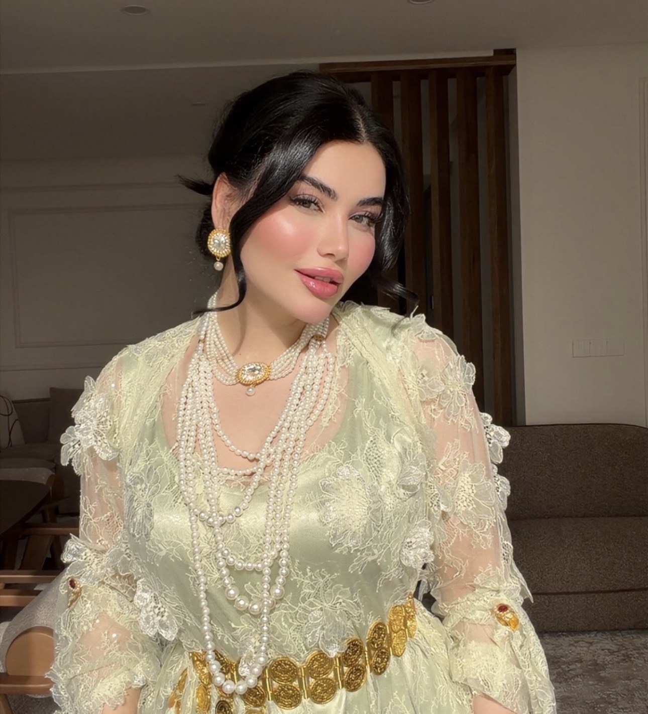 Pale green lace dress worn with strands of pearls at the neck and a gold coin belt at the waist
