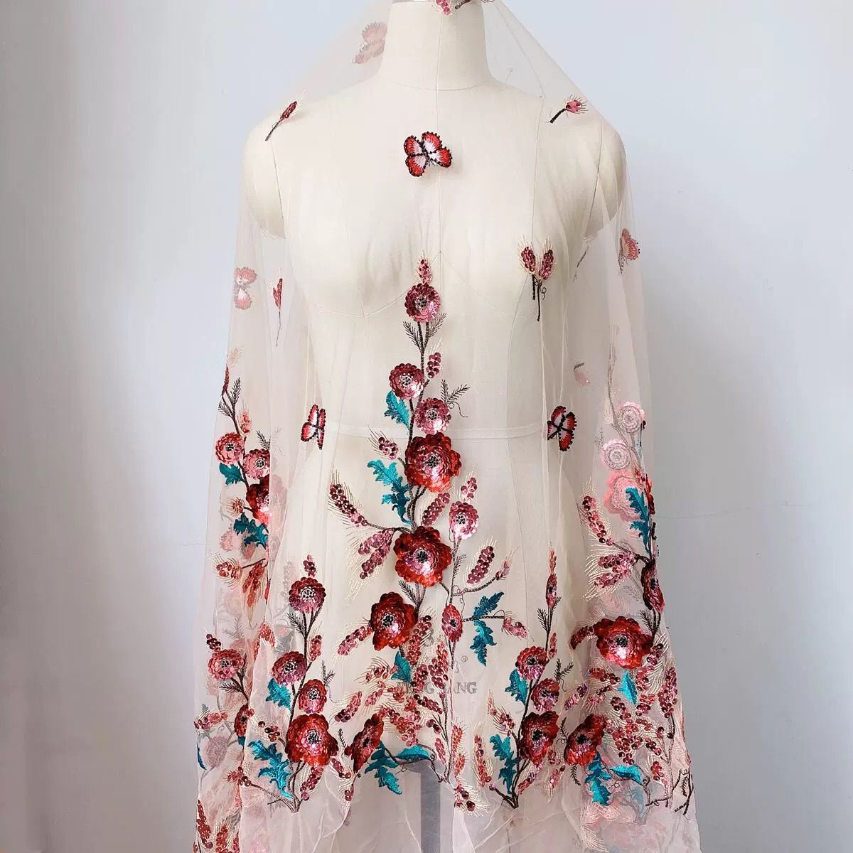 Tulle embroidered with red and teal sequin flowers, draped on a dress form